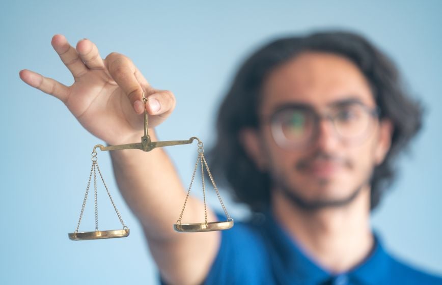 Person holding a small brass balance scale toward the camera.