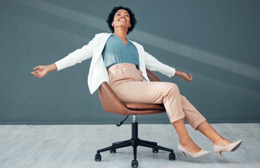 Smiling woman leaning back in an office chair with arms outstretched.