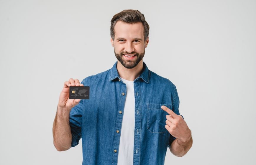 Smiling man pointing to a credit card he’s holding.