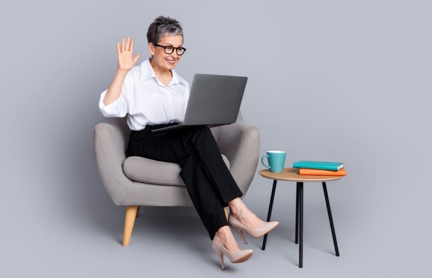 Woman sitting in a chair using a laptop and waving during a video call