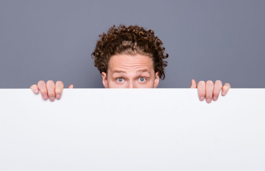Man peeking over a blank white sign.